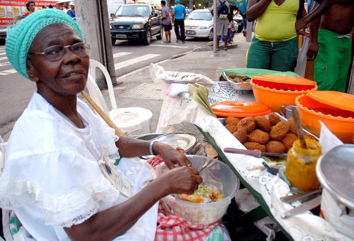 Além da culinária, a Baiana do Acarajé é símbolo da resistência afro-brasileira. Sua história entrelaça fé, ancestralidade e luta pela liberdade, visto que os bolinhos de feijão com dendê financiaram terreiros e cartas de alforria. Assim, ser baiana do acarajé é profissão centenária, feminina e sagrada, concedida pelos orixás. -  (crédito: wikimedia commons Rodrigues Pozzebom)