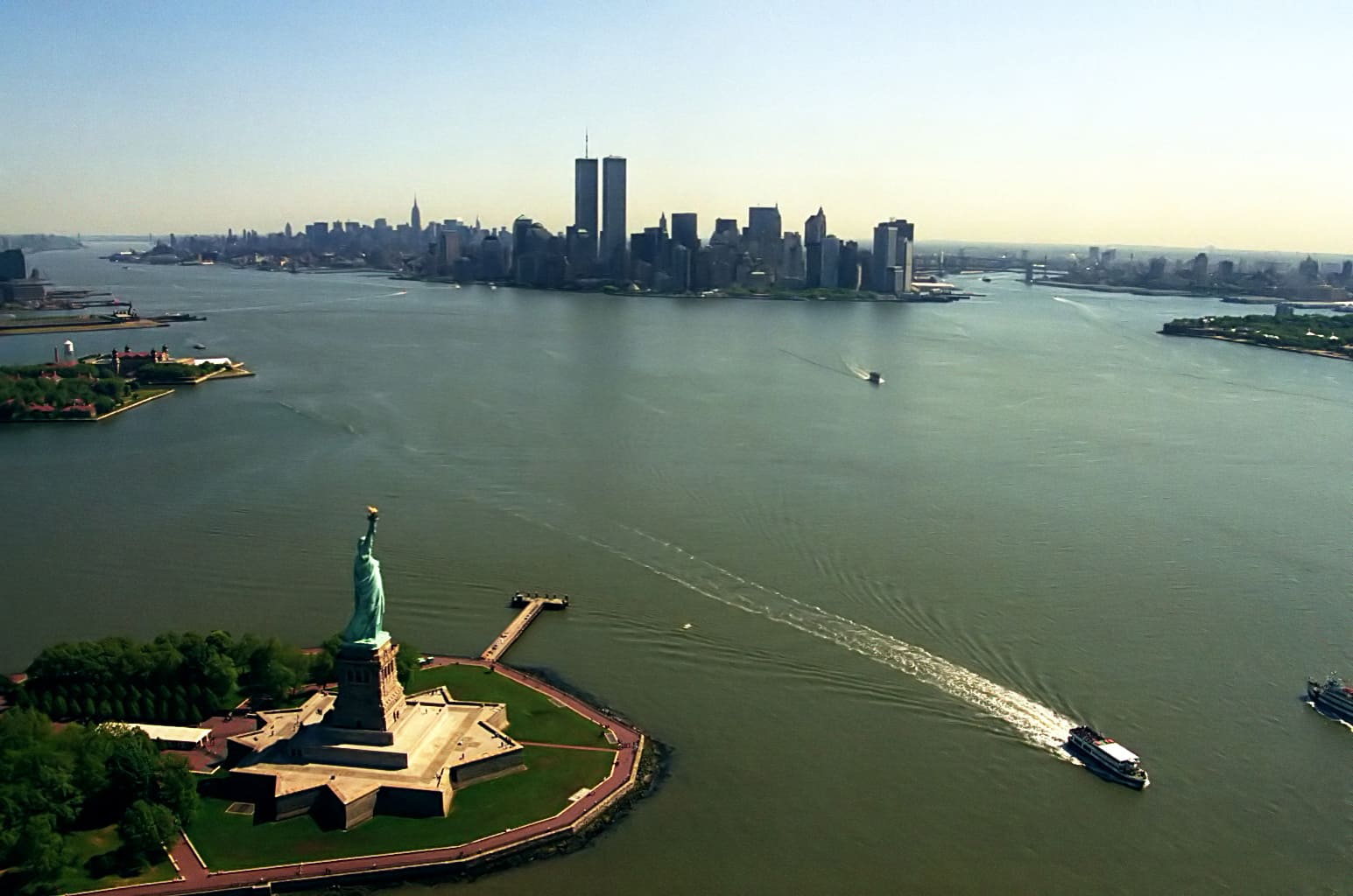 As Torres Gêmeas eram um marco na paisagem de Manhattan, sendo vistas de longe devido ao seu gigantismo. Na imagem, uma panorâmica em que se percebe a Estátua da Liberdade em primeiro plano e as torres ao fundo. t - Germán Ramos ? Domínio público 