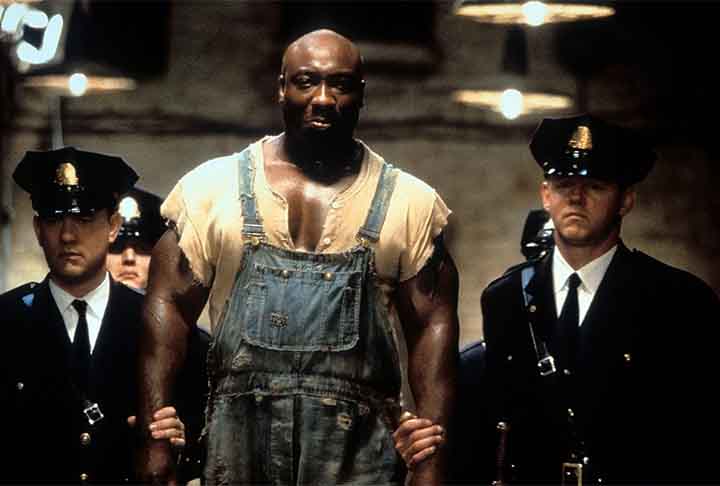 À Espera de um Milagre (1999): dirigido por Frank Darabont, é um drama baseado na obra de Stephen King que se passa na década de 1930 em uma prisão. A história segue Paul Edgecomb (Tom Hanks), um guarda do corredor da morte, que se depara com John Coffey (Michael Clarke Duncan), um prisioneiro condenado por um crime horrendo. No entanto, Coffey revela ter habilidades sobrenaturais e uma natureza gentil, desafiando as percepções de Edgecomb sobre justiça e humanidade. - Divulgação