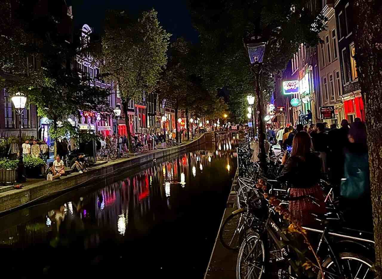 Red Light District (De Wallen) - Descrição: O bairro mais famoso de Amsterdã, conhecido por suas vitrines iluminadas em vermelho, tem uma história que remonta ao século XIV. Hoje, é uma área regulamentada e culturalmente significativa - Localização: Centro de Amsterdã - Referências Históricas: De Wallen é um dos distritos mais antigos e preservados da cidade