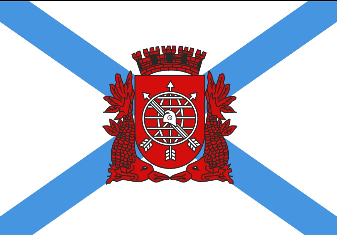 A bandeira da cidade do Rio de Janeiro consiste em um retângulo branco com duas faixas diagonais azuis se entrecruzando, com o Brasão da cidade, na cor vermelha, no centro.-Domínio público 