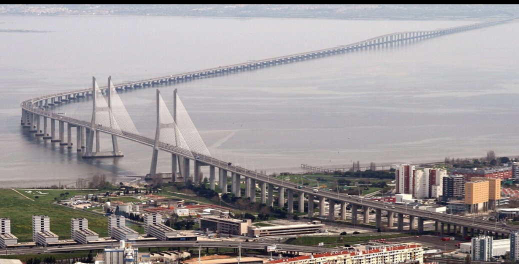 A Ponte Vasco da Gama, em Portugal, foi inaugurada em 29/3/ 1998, dois meses antes da abertura da ExposiÃ§Ã£o Mundial. O seu nome comemora os 500 anos da chegada de Vasco da Gama Ã  Ãndia, em maio de 1498.. Tem 17, 185 km  sobre o rio Tejo.-
