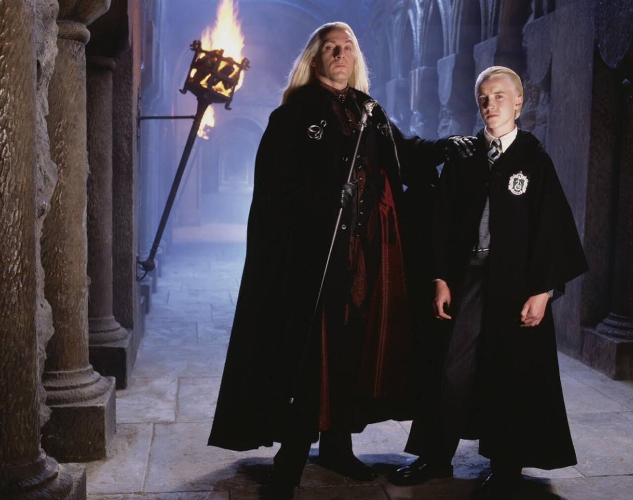Foi então que Isaacs sugeriu um visual mais extravagante e condizente com a nobreza bruxa: uma capa de pele ou veludo e, acima de tudo, uma longa peruca loira. A proposta não só redefiniu Lucius Malfoy como também se tornou uma marca registrada do personagem.
