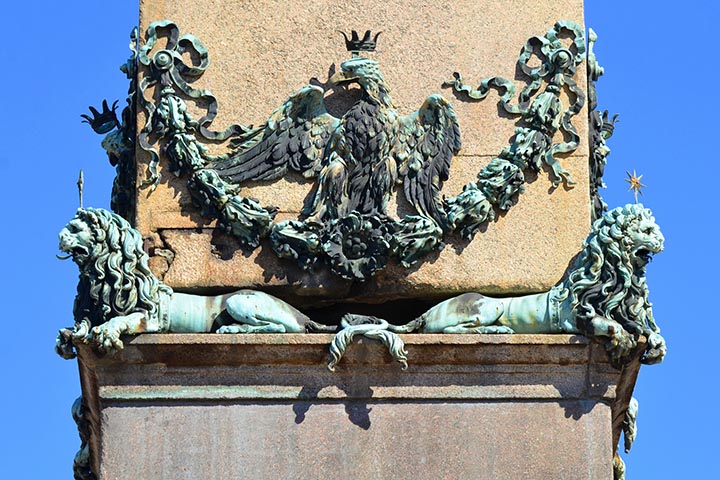 A base do obelisco é adornada por quatro leões de bronze, símbolos de força e vigilância. Esses elementos reforçam a imponência da estrutura e criam uma conexão entre o poder imperial romano e a simbologia cristã. O conjunto transmite a ideia de que o monumento guarda e protege a memória dos mártires.