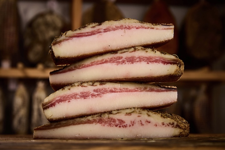 <p>É feito a partir de um corte diferente: a bochecha ou papada do porco. Essas partes costumam ter uma proporção de gordura muito maior e uma textura mais firme e amanteigada do que a carne da barriga.</p>
