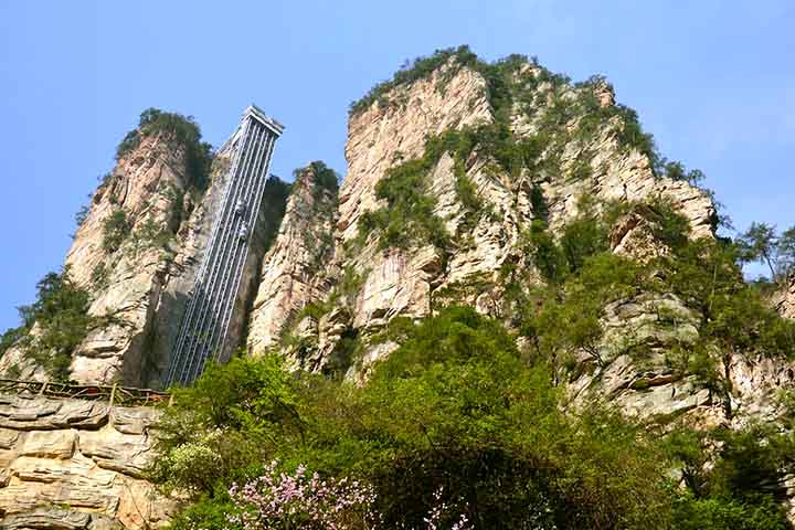 O Elevador dos 100 Dragões, o Bailong Elevator, é uma das atrações mais impressionantes de Zhangjiajie. Construído diretamente na face de um penhasco, ele é considerado o maior e mais alto elevador ao ar livre do mundo, com altura de 326 metros. Inaugurado em 2002, revela engenharia moderna que permite aos visitantes subirem em menos de dois minutos até miradouros.  