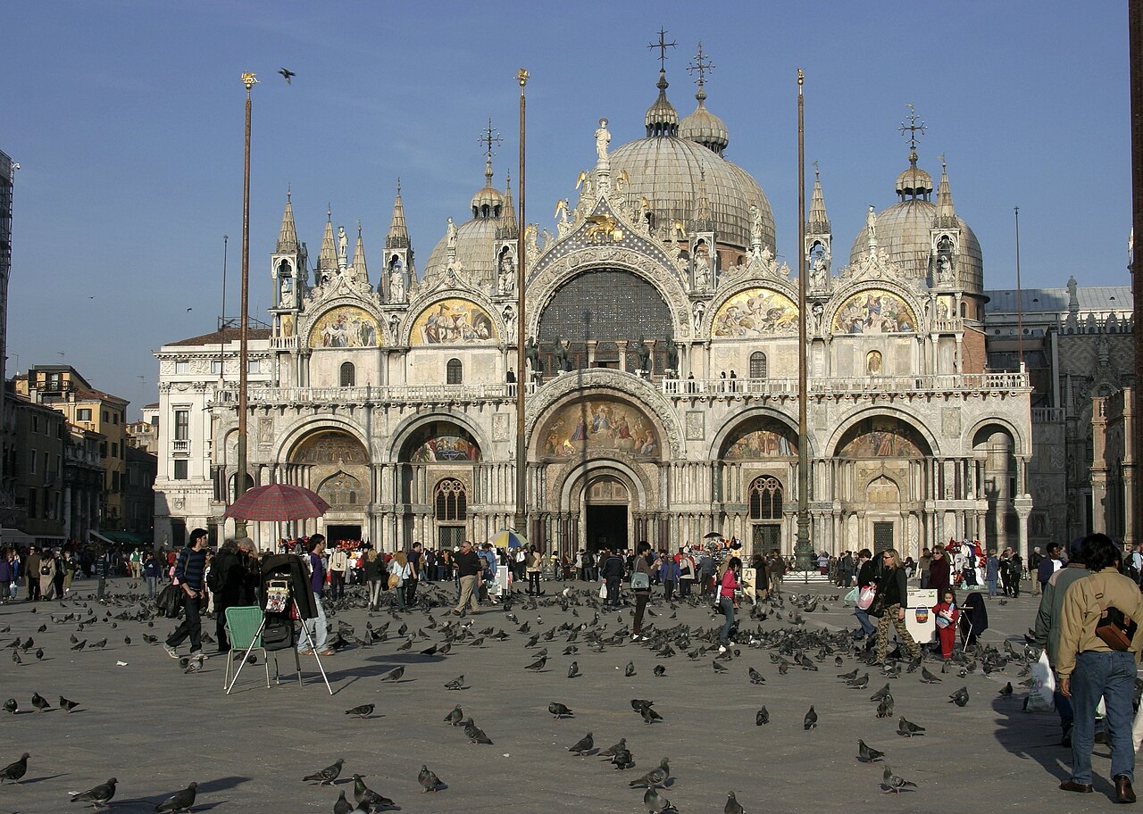 A Basílica de São Marcos, aliás, é o monumento mais emblemático da praça, construída no estilo bizantino com mosaicos dourados que impressionam pela riqueza. Originalmente capela privada do doge, tornou-se símbolo religioso e político da cidade. Sua arquitetura resulta das conexões comerciais de Veneza com o Mediterrâneo.
