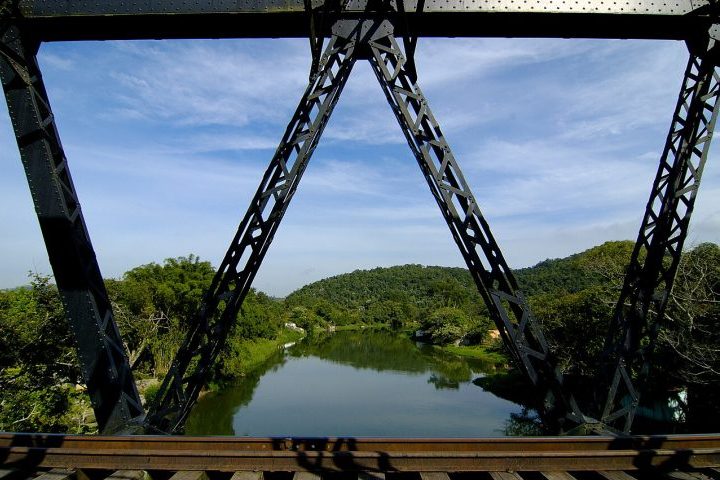 Além da fé, a engenharia do início do século passado também deixou marcas profundas na identidade visual da região. Um imponente pontilhão de ferro, montado por técnicos ingleses em 1910, atravessa as águas do rio e serve hoje como um cenário privilegiado para registros fotográficos.