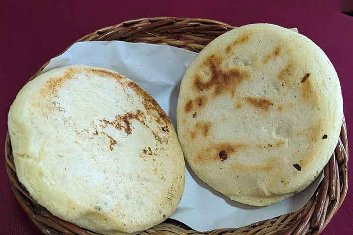 Embora venezuelanos e colombianos disputem historicamente a origem do prato, pesquisadores apontam que a arepa já era produzida por povos indígenas muito antes da chegada dos colonizadores europeus à América do Sul. O nome teria origem na palavra “erepa”, utilizada por indígenas da etnia cumanagoto para designar o milho. Ao longo dos séculos, a receita foi sendo adaptada, mas manteve sua essência simples: água, sal e milho transformados em uma espécie de pão circular.
