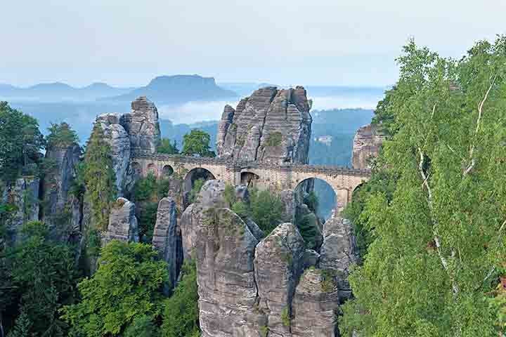 O Parque Nacional da Suíça Saxônica, vizinho a Königstein, é famoso por suas formações rochosas e trilhas deslumbrantes, incluindo miradouros como a Ponte Bastei, que oferece vistas espetaculares do vale do Elba. A diversidade natural atrai amantes de esportes ao ar livre e fotógrafos, enquanto a cidade integra turismo cultural e ecológico em todas as estações. No verão, trilhas e passeios de barco são populares, e no inverno a paisagem ganha charme especial, reforçando Königstein como destino c