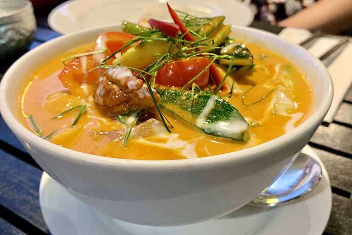 Já a Assam Laksa, típica da ilha de Penang, na Malásia, possui características bastante diferentes. O caldo é preparado à base de peixe e tamarindo, ingrediente responsável por um sabor ácido bastante característico. Nessa versão, ervas aromáticas, hortelã, cebola roxa, pepino e pasta de camarão fermentado ajudam a criar uma combinação considerada mais intensa e complexa. Para muitos especialistas em gastronomia asiática, a Assam Laksa está entre os pratos mais icônicos da culinária malaia.
