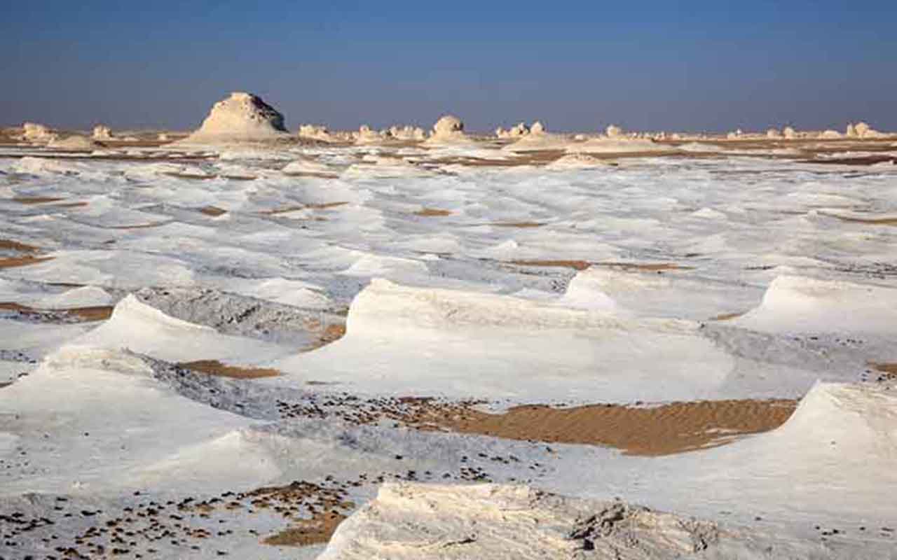 O Deserto Branco, localizado na região de Farafra, é um dos cenários mais impressionantes do Egito e atrai visitantes de todo o mundo. Suas formações rochosas de giz criam paisagens surreais, lembrando esculturas naturais moldadas caprichosamente pelo vento e pela areia. A beleza única do lugar contrasta com o céu azul intenso e o silêncio profundo do deserto. Além de ser um espetáculo visual, o Deserto Branco guarda importância geológica e histórica para o país. As rochas esculpidas ao longo de -  (crédito:  Divulgação)