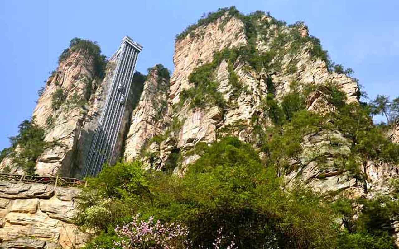 O Elevador dos 100 Dragões, o Bailong Elevator, é uma das atrações mais impressionantes de Zhangjiajie. Construído diretamente na face de um penhasco, ele é considerado o maior e mais alto elevador ao ar livre do mundo, com altura de 326 metros. Inaugurado em 2002, revela engenharia moderna que permite aos visitantes subirem em menos de dois minutos até miradouros.  