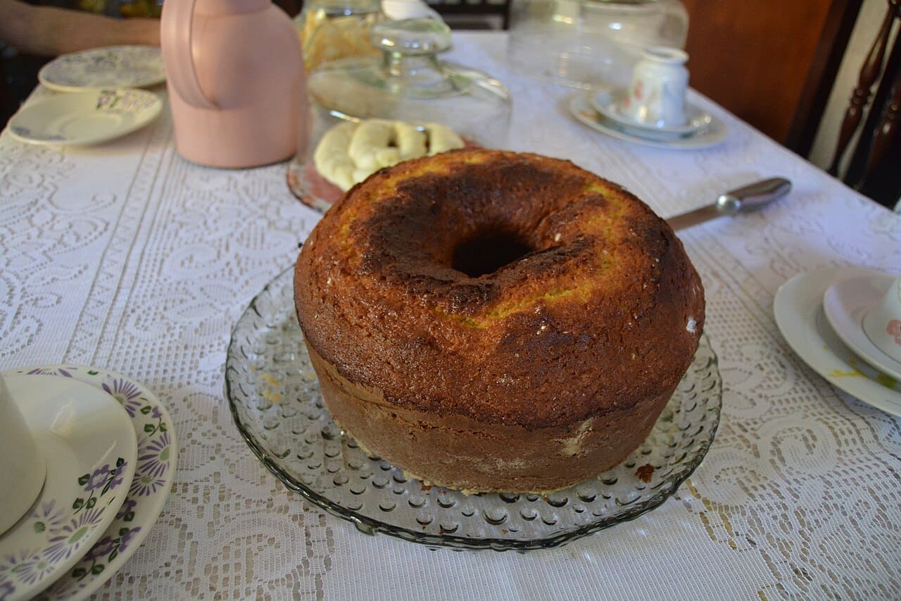 O bolo de fubá é um clássico das quermesses, feito com farinha de milho, leite e ovos, resultando em textura leve e sabor inconfundível. Nas festas, é servido em fatias generosas, acompanhado de café ou vinho quente, reforçando o clima acolhedor. Sua simplicidade encanta e sua tradição atravessa gerações, mantendo viva a memória afetiva das festas juninas.