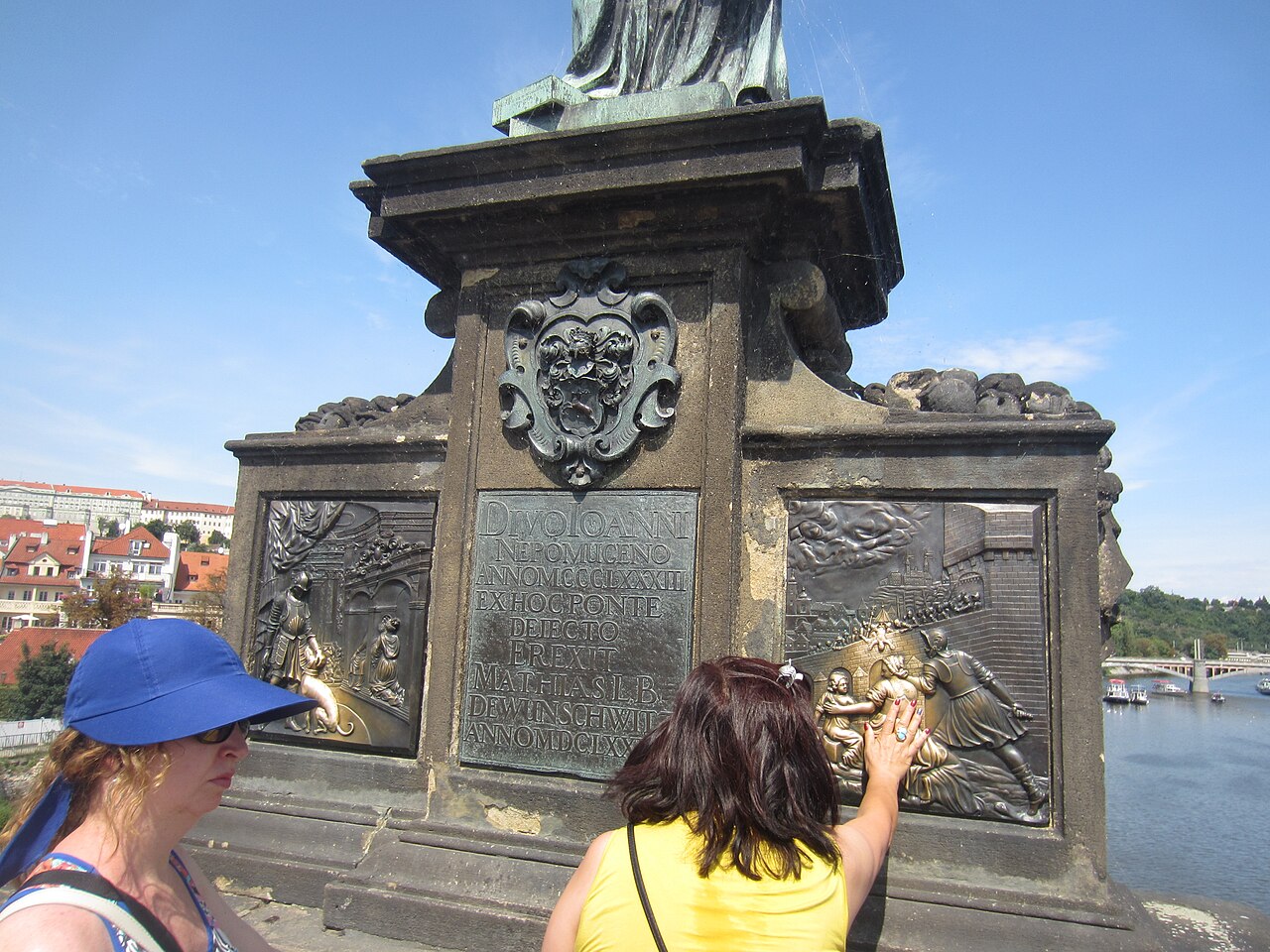 Existe uma tradição muito conhecida relacionada a essa estátua. No pedestal de bronze há dois baixos-relevos que retratam cenas da vida do santo. Segundo a crença popular, os visitantes que tocarem com a mão direita a cena que representa seu martírio terão boa sorte e um dia retornarão a Praga. Com o passar do tempo, esse costume desgastou o bronze nessas áreas específicas, tornando-as visivelmente mais brilhantes e polidas do que o restante da escultura. 