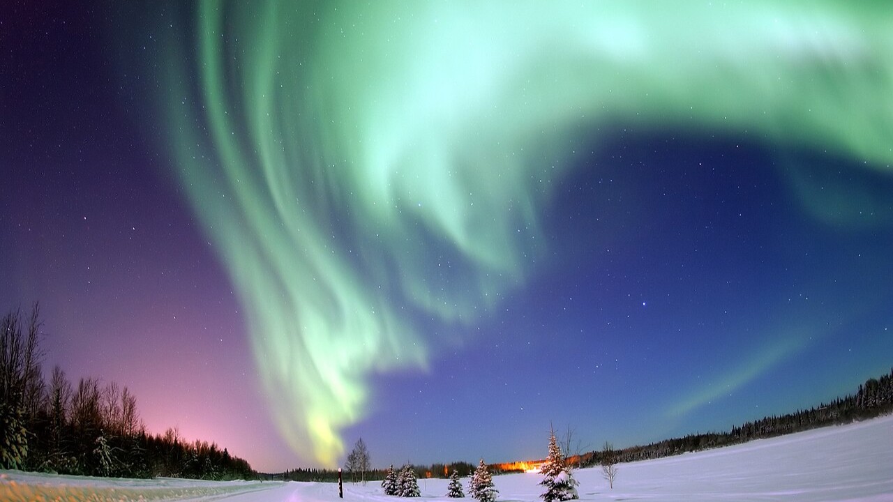 Mas afinal, o que é a aurora boreal? A aurora boreal é um fenômeno natural formado por faixas de luz coloridas que dançam no céu noturno, que são resultado de quando partículas carregadas vindas do Sol, transportadas pelo vento solar, colidem com gases presentes na atmosfera terrestre, como oxigênio e nitrogênio. Esse encontro libera energia em forma de luz.
