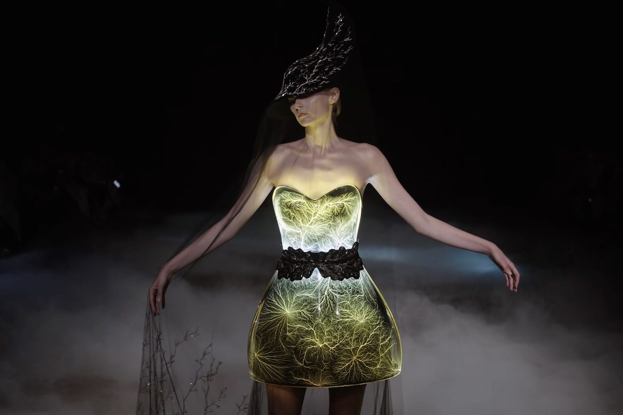 Outro lançamento marcante foi o vestido 'Universo Fractal', criado com o auxílio de um acelerador de partículas em condições extremas de temperatura (-100°C). O processo resultou em uma peça capaz de reter elétrons e gerar intensas descargas elétricas visíveis, explorando os limites entre a matéria, a energia e o corpo. -  (crédito: Reproduc?a?o/YouTube Iris van Herpen )
