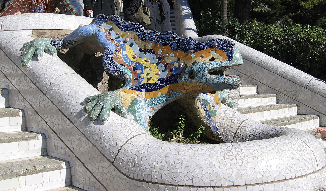 O dragão, também chamado de salamandra, é um dos símbolos mais fotografados do Parque Güell. Construído com a técnica de trencadís, mosaicos feitos de fragmentos cerâmicos, ele brilha em cores vivas. Localizado na escadaria principal, tornou-se ícone da cidade. Representa a força da natureza e a imaginação sem limites de Gaudí. É parada obrigatória para qualquer visitante.