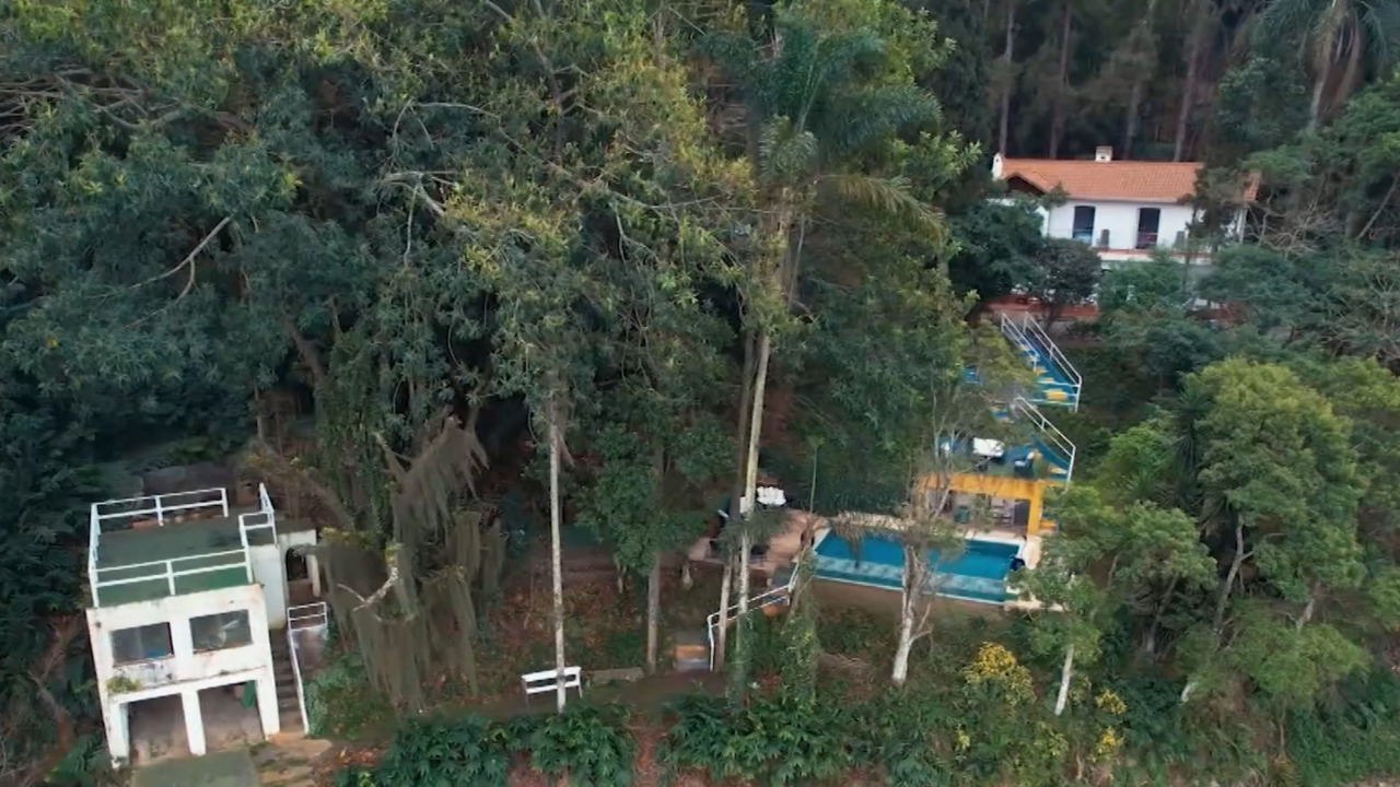 Na parte externa, a propriedade conta com piscina e deck em meio à área verde. A piscina fica em um dos níveis mais baixos do terreno, abaixo da residência, e o jardim conta com plantas coloridas e distribuídas pelos diferentes espaços, que acompanham os desníveis do relevo. 
