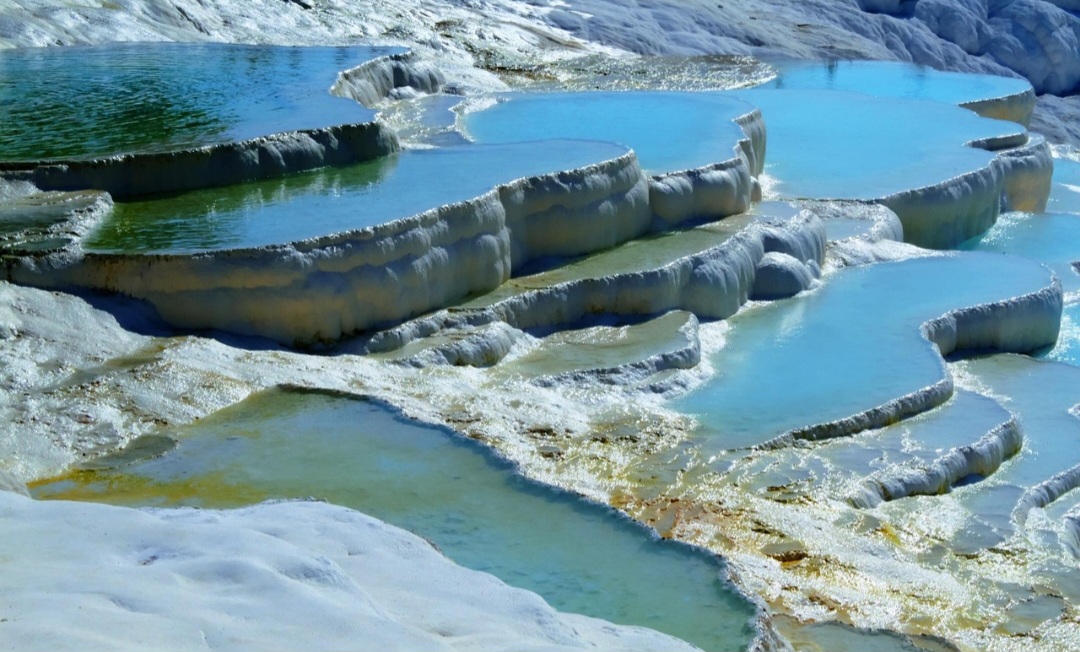 A aparência de Pamukkale resulta da ação de águas termais ricas em bicarbonato de cálcio. Quando chegam à superfície, parte do dióxido de carbono dissolvido é liberada, favorecendo a precipitação de carbonato de cálcio. Esse mineral se acumula e forma o travertino, rocha responsável pela coloração branca dos terraços.